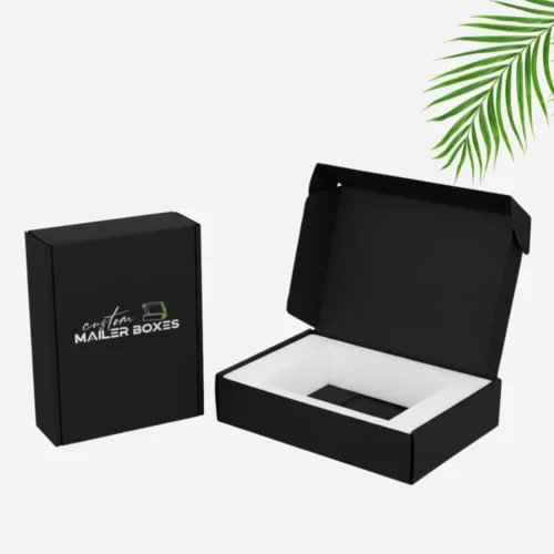 A closed black laptop mailer boxes with the "Custom Mailer Boxes" logo in white is shown next to an open black mailer box. The open box contains white foam inserts, indicating space for a product.