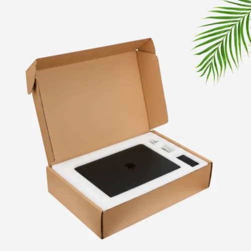 An open cardboard mailer box contains a black laptop, a white charging cable, and a black power adapter, all nestled in white foam inserts.
