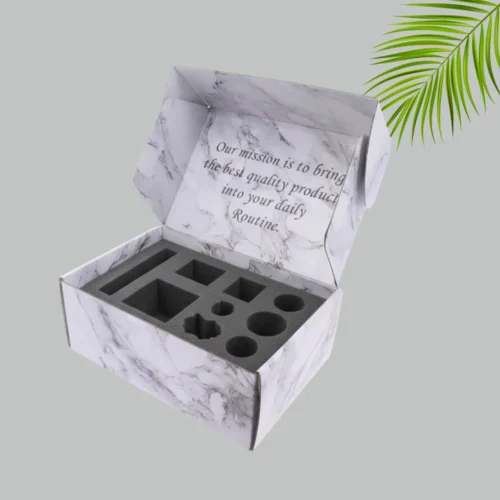 An open marble-patterned mailer box with black foam inserts designed to hold various products securely. The inside lid has printed text: "Our mission is to bring the best quality product into your daily Routine."