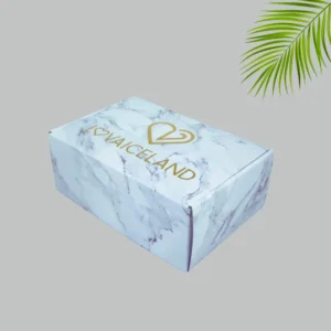 A closed rectangular mailer box with a white marble design. The lid displays a gold heart-shaped logo above the brand name in bold gold lettering.