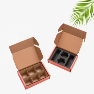 Two open pink mailer boxes are shown at an angle. The box on the left has cardboard dividers creating six compartments. The box on the right has a black foam insert with two round sections and two oblong sections for holding products.