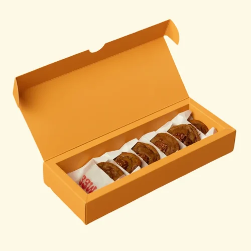 Long orange cookie mailer box, shown open with white tissue paper holding five round cookies, ideal for packaging baked goods for delivery or sale.