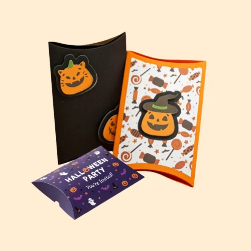A set of three pillow-style Halloween party boxes/invitations: one black with a pumpkin sticker, one with an orange pumpkin and sweets pattern, and a small purple box reading "HALLOWEEN PARTY You're Invited.