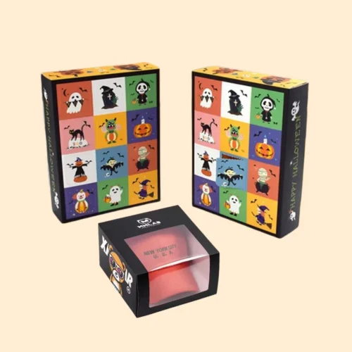 A 3D mockup of three spooky Halloween boxes: two vertical cartons featuring a multicoloured grid of cartoon ghosts and pumpkins, and a small black window box displaying a red fabric product.